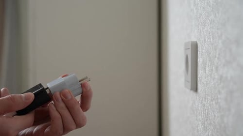 Seitenansicht einer nicht erkennbaren Person, die vorsichtig einen weißen und schwarzen Stecker in die Wand steckt