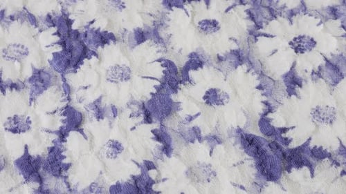 Top view of the light textured lace fabric in white and lilac tones with a floral pattern rotates