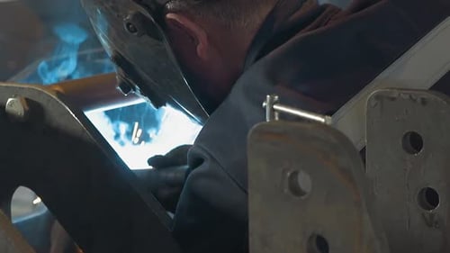 Employee with Protective Mask Welds Metal Frame in Workshop