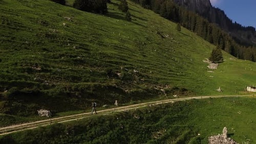 Aerial drone shot, backpacker hiking on mountain cliffside dirt trail during summer