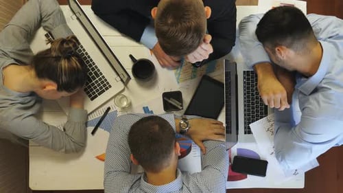 Vista superior de colegas cansados que se duermen sobre una mesa con computadoras portátiles y documentos en la oficina
