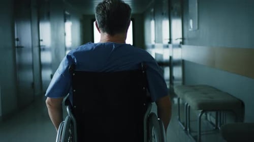 In the Hospital, Front View Following Shot of the Elderly Man in the Wheelchair Moving through the