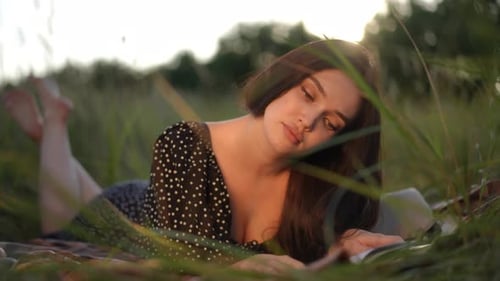 Slow Motion Cute Girl Enjoys Reading a Book While Lying in Front on a Plaid in Tall Green Grass in a