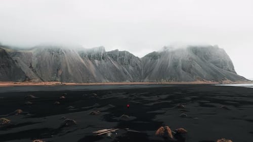 Cinematic 4K Aerial video of a mountain in Iceland with a man walking on the Black Sand Beach