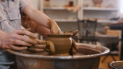 Focuced close up view. Using the pottery wheel to shape the clay. Mother is with little girl