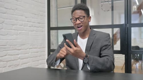 Young African Man Celebrating Success on Phone in Office