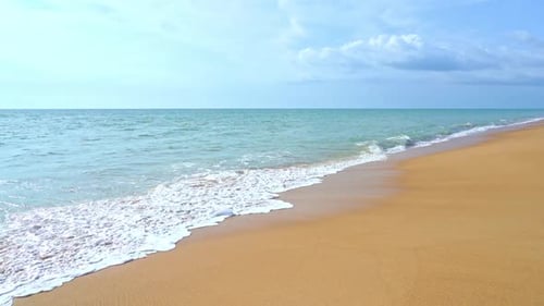 Foam of waves crashing on golden sandy empty deserted beach. Slow-motion