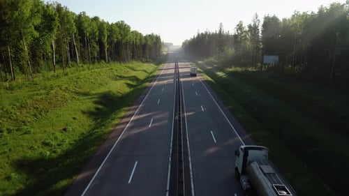 Gasoline truck is driving down a straight highway in the woods.