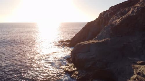 Amazing aerial view of rugged sea coastline, bright golden hour sky, forward