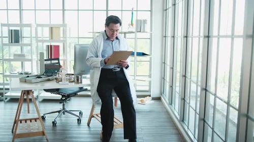 Mature Male Doctor Reviewing Medical Records in a Sunlit Office