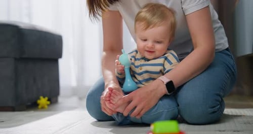 Ein fröhliches Baby, das auf dem Boden sitzt und eine erwachsene Pflegekraft beim Spielen in der Hand hält und interagiert