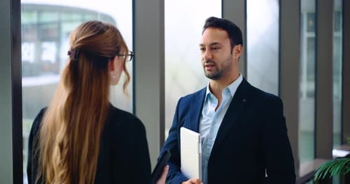 Caucasian business man and woman discussing project standing near modern office windows