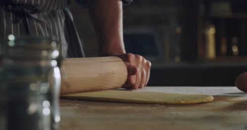 Cinematic close up shot of professional artisan baker chef rolling dough for preparation of pasta,