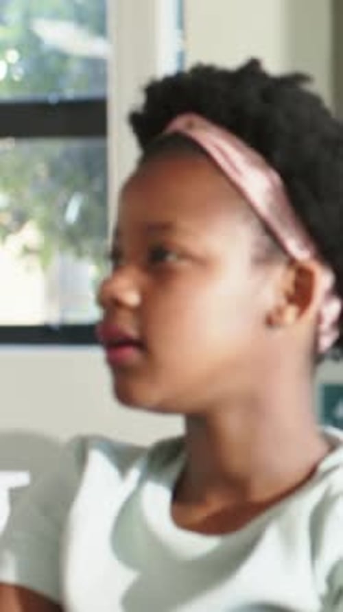 Vertical video: Turning student answering offscreen voice at desk by window, wearing pink headband