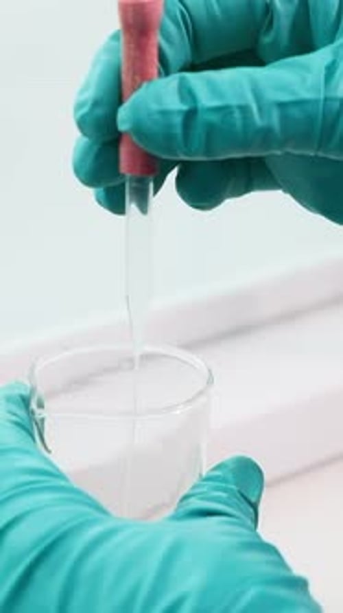 Close Up of Transparent Liquid Being Poured Into a Bottle with a Pipette on a White Background Clip