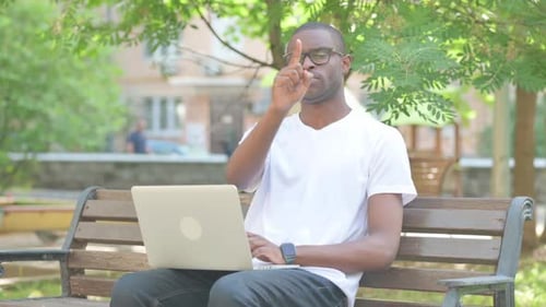Hombre afroamericano con una computadora portátil apuntando a la cámara mientras está sentado al aire libre