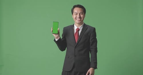 Asian Business Man With A Smile Showing Green Screen Mobile Phone On Green Screen Studio