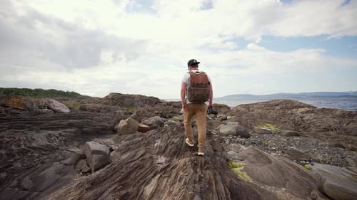 Man Hiking on Rocky Coastline with Camera