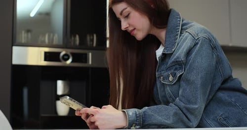 Attraktive Frau, die in der Küche eine SMS-Nachricht auf dem Smartphone schreibt und soziale Medien zu Hause scrollt