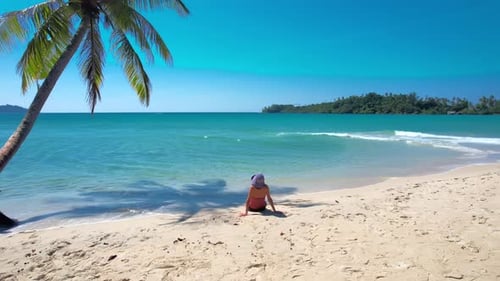 Rear view of young woman traveler sitting outdoors peacefully on the sand.