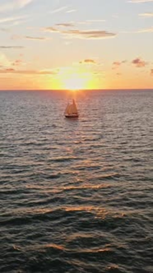 Sailboat illuminated by golden sunset on rippling ocean horizon