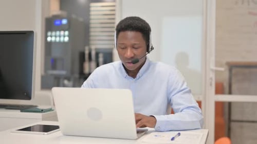 African Man with Headset Doing Video Chat on Laptop in Call Center