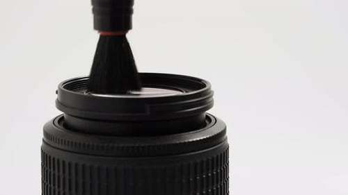 A lens cleaning brush cleans the lens on a white background. Close-up.