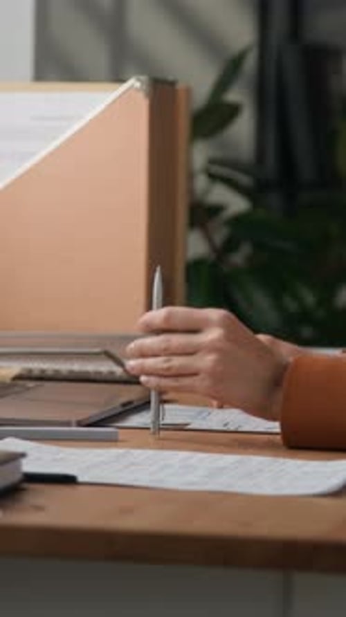 Office Employee Tapping Pen on Wooden Desk While Doing Paperwork