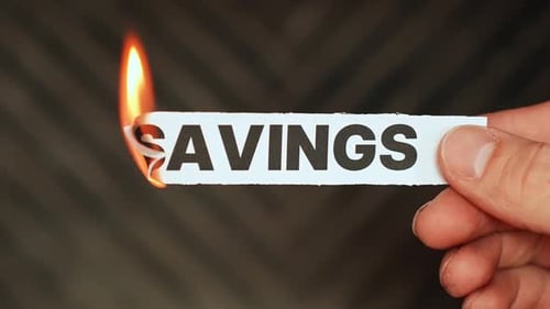 Burning “savings” label held by hand, symbolizing depleted savings, emergency spending, financial