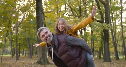 Grandfather Holding Granddaughter Piggyback in Autumn Park