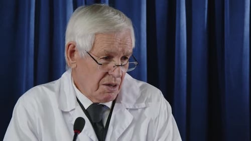 Senior Man in Lab Coat Speaking at Microphone