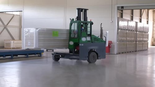 Carretilla elevadora de almacén: transporte Una carretilla elevadora se mueve a lo largo de un pasillo de almacén levantando una buena caja