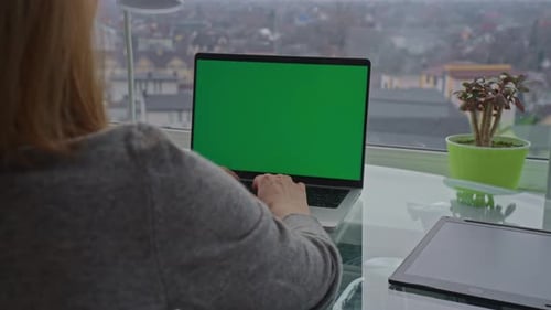 Woman Typing on Laptop with Green Screen by Window