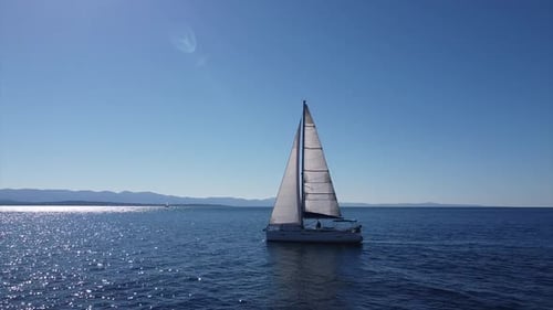 Sailboat on open ocean filmed by drone doing ha 180 degrees turn camera sun frontal to side Croatia