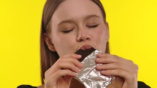 Woman Eating Chocolate on a Yellow Background