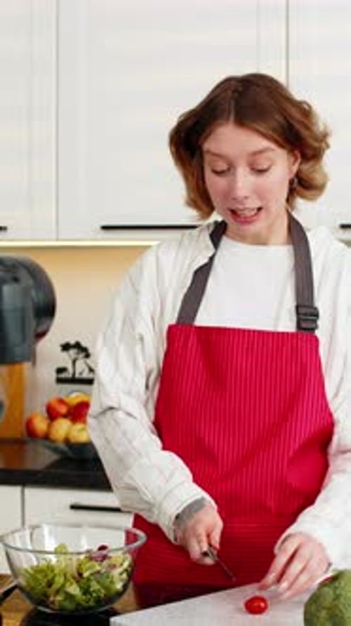 Mujer joven que prepara una ensalada saludable para cocinar en un vlog mientras habla con la cámara en la rutina de la cocina de su casa
