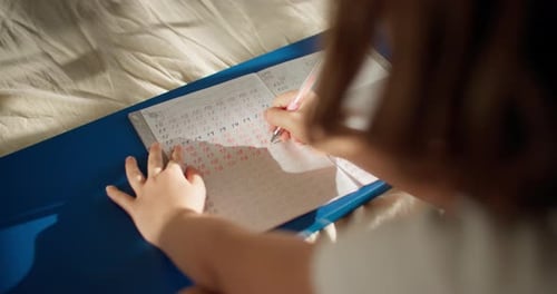 Child Writes In Workbook With a Pink Pen