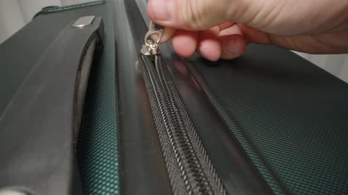 A Hand zips up the suitcase and secures the zipper pulls in the lock, finalizing preparations before