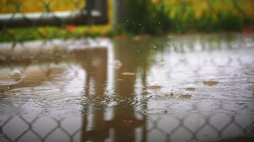 Gotas de chuva caindo do céu e caindo em uma poça de quintal perto de uma cerca ou portão de arame - sl