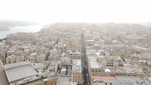 Drone flies sideway to the right over the main street of Malta with Basilica in the haze