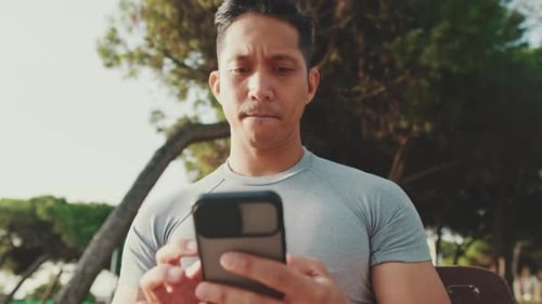 Young man sitting on a park bench uses a mobile phone