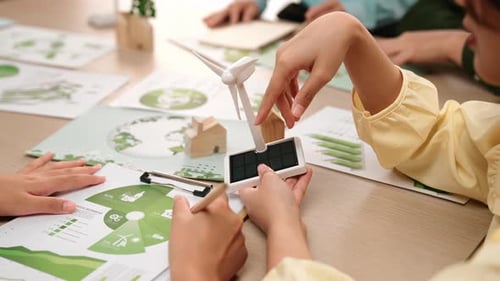 Business team with green energy graph and windmill model on table. Delineation.