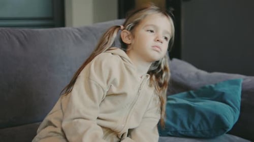 Sad Girl Sitting on Couch in a Cozy Living Room Wearing a Beige Hoodie and Looking Contemplative