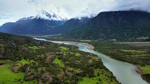 Aerial drone view of a winding river surrounded by green valleys and dramatic snow covered peaks in