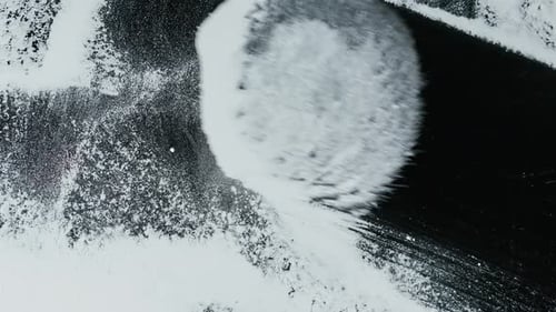 Large fluffy brush wipes snow or white powder from a transparent surface, filming from below