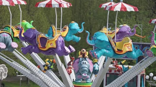 A marry-go-round with elephant-shaped seats in the amusement park. Slow-motion, parallax shot.