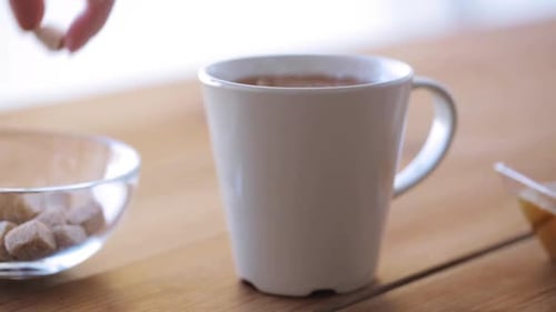 Unhealthy Eating and Drinks Concept - Hand Adding Sugar to Cup Of