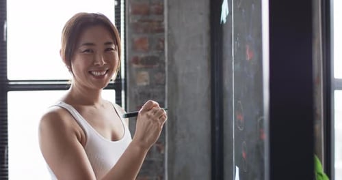 Woman Smiling and Writing on Chalkboard in Office
