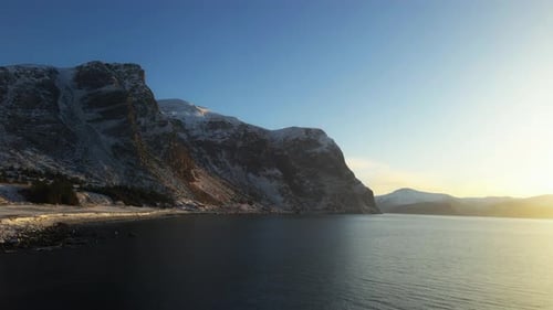 Scenic drone shot of high mountains covered with snow at the water's edge in Norway with a bright