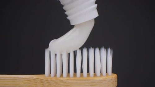 Super close-up camera shot of toothpaste dropping on the toothbrush. White toothpaste. Probe lens.